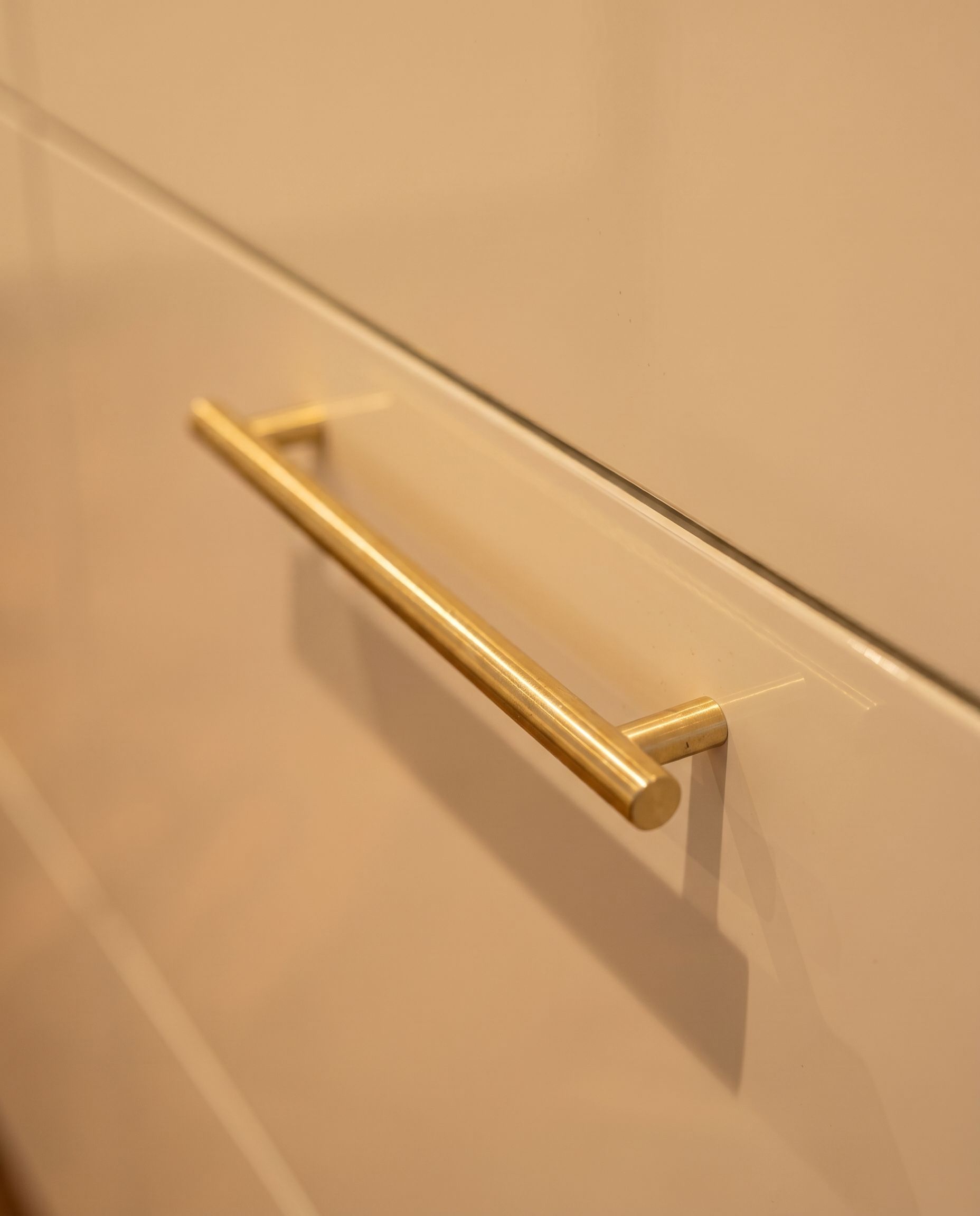 Detailaufnahme der elfenbeinfarbenen Hochglanzfronten mit Messing-Griffleiste in Eislingen.